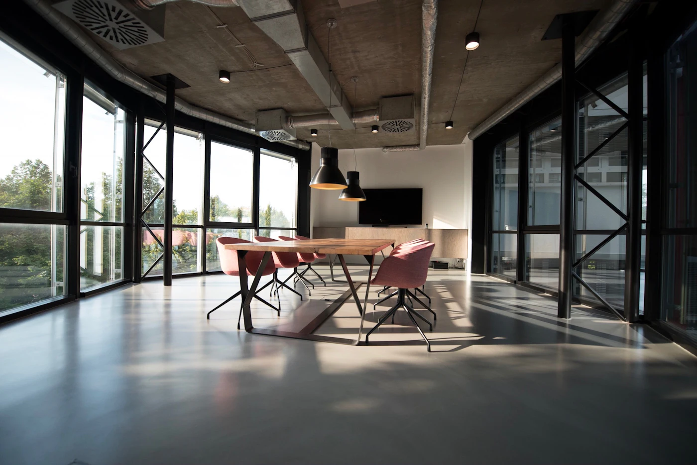 Open commercial office with exposed concrete ceiling, black window frames, and a conference table